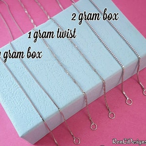 May include: Five silver chains of different styles and lengths on a blue background. The chains are labeled "1 gram box", "1 gram twist", and "2 gram box".