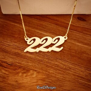 May include: Gold necklace with a cursive '222' pendant.
