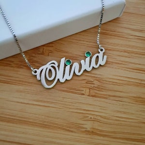 May include: Silver necklace with the name Olivia spelled out in cursive with two green gemstones.
