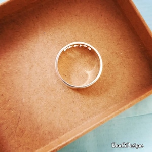 May include: A silver-colored metal ring featuring a cut-out design along the upper band. The ring has a smooth, polished finish and a circular shape. The text RonLiDesigns is visible in the bottom right corner of the image.