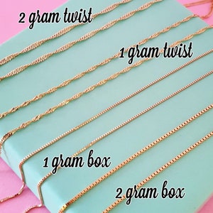 Könnte beinhalten: Nahaufnahme mehrerer goldfarbener Kettenhalsketten. Das Bild zeigt zwei Stile: Twist- und Box-Ketten, jeweils in 1- und 2-Gramm-Gewichten. Der Text "2 gram twist", "1 gram twist", "1 gram box" und "2 gram box" ist sichtbar.