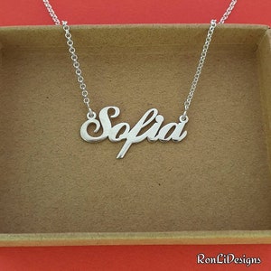 May include: Silver necklace with the name "Sofia" spelled out in a cursive font.