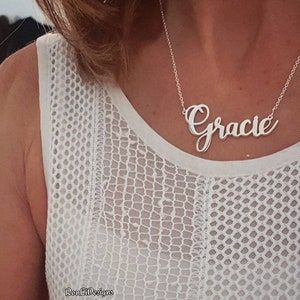 Peut inclure: Un collier en argent avec le nom "Gracie" écrit en cursive. Le collier est porté par une personne portant un haut blanc en dentelle.