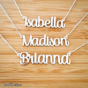 May include: Three silver necklaces with personalized names: Isabella, Madison, and Brianna. The necklaces are on a wooden background.