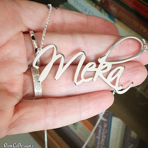 Könnte beinhalten: Silberkette mit einem Anhänger mit dem Namen "Meka" in Schreibschrift.