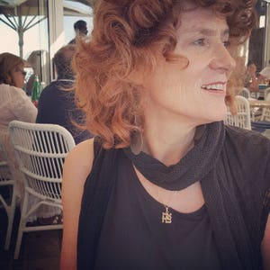 Peut inclure: Une femme aux cheveux roux bouclés portant un haut noir et une écharpe noire avec un collier à pendentif en or. Le pendentif est un petit motif complexe.