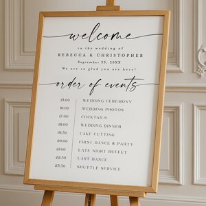 May include: A wooden easel displaying a wedding welcome sign. The sign features elegant calligraphy with the names Rebecca & Christopher and the date September 25, 20XX. Below, a schedule of events is listed, including the wedding ceremony, dinner, and dance.