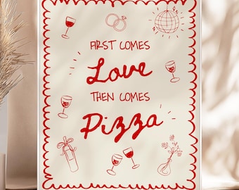 May include: A framed print with a red scalloped border features the text "First Comes Love Then Comes Pizza" in red script. The print includes red illustrations of wine glasses, rings, and a disco ball. A vase with dried plants is to the left.