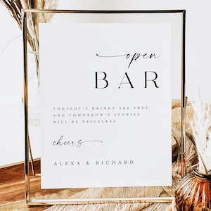May include: A rectangular gold metal frame holding a white sign with black text that reads open BAR, TONIGHT'S DRINKS ARE FREE AND TOMORROW'S STORIES WILL BE PRICELESS, cheers, and ALEXA & RICHARD, displayed in a clear glass holder with a thin metallic edge.