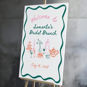 May include: A white sign on a wooden easel with a green border. The sign reads "Welcome to Samantha's Bridal Brunch" in pink and green. A drawing of brunch items and the date July 18, 2028, are also featured.