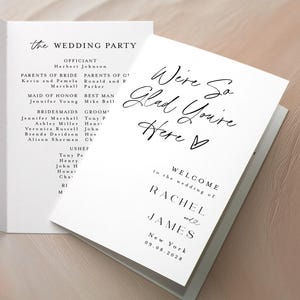 May include: White wedding programs with black text, displaying ceremony details, wedding party information, and a welcome message. The programs are open on a light-coloured surface. The programs are made of paper.