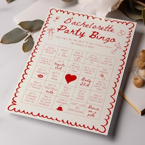 Op de afbeelding: Een rechthoekige Bachelorette Party Bingo spelkaart met een rode geschulpte rand. De kaart bevat rode tekst en iconen, waaronder een wijnglas, ringen en een hart. Het raster bevat diverse feestuitdagingen geschreven in rode inkt.