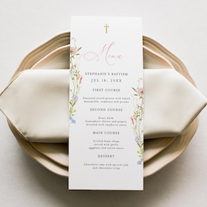May include: A baptism menu card with floral decorations, featuring the word "Menu" in pink script. The card lists courses like roast duck and chocolate cake, and is set on a wooden plate with a folded napkin.