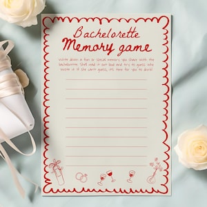 May include: A white gift box with a cream ribbon, a Bachelorette Memory Game card, and two white roses. The card has a red scalloped border and text that reads "Bachelorette Memory game".