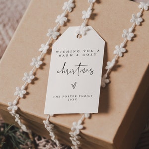 May include: A brown gift box wrapped with white lace and a white gift tag. The tag has the text "Wishing you a warm & cozy christmas" with a heart symbol and "The Foster Family 20XX".