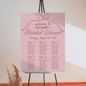 May include: A pink bridal shower seating chart with a handwritten title "Welcome to Elizabeth's Bridal Shower" and the date "Saturday, August 20, 2028". The chart lists tables with guest names.