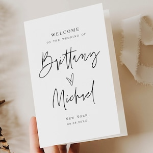 May include: A white wedding welcome card featuring black text that reads Welcome to the wedding of Brittany and Michael, with a small heart symbol between the names, followed by New York and the date 09.08.20XX in a clean, modern font style.