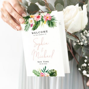 Op de afbeelding: Een huwelijksuitnodiging met een tropisch thema. De uitnodiging heeft een aquarel-illustratie van roze en witte bloemen, groene bladeren en een palmblad. De tekst op de uitnodiging luidt "Welkom op de bruiloft van Sophia & Michael, New York, 09.08.2022".