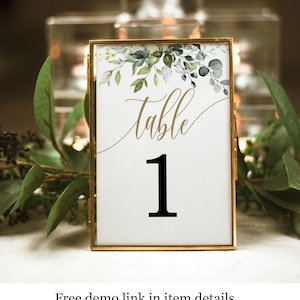 May include: A gold-framed table number card with a watercolor design of green leaves and the text "table 1" in black.