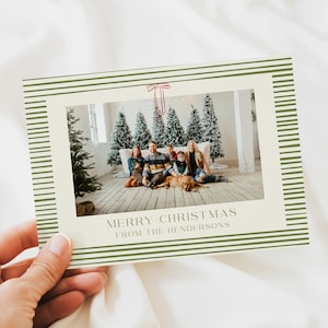 Op de afbeelding: Een kerstkaart met een familiefoto in een crèmekleurige lijst. De lijst heeft groene horizontale strepen. De tekst "MERRY CHRISTMAS FROM THE HENDERSONS" staat onderaan de foto.