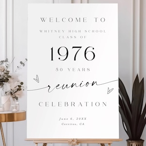 May include: A white rectangular sign on a wooden easel featuring black text that reads Welcome to Whitney High School Class of 1976 50 Years Reunion Celebration, June 6, 20XX, Cerritos, CA, with two small hand-drawn heart outlines.