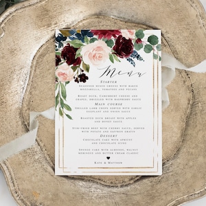 May include: A wedding menu card with a floral design featuring burgundy, pink, and blue flowers. The menu includes starter, main course, and dessert options. The text reads "Menu", "Starter", "Main Course", "Dessert", "Kate & Matthew".