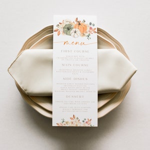 Op de afbeelding: Een Thanksgiving-menu met een aquarelillustratie van pompoenen en herfstbladeren. Het menu bevat een voorgerecht, een hoofdgerecht, bijgerechten en een dessert. De tekst luidt: "menu", "Eerste gang", "Gebakken brie met cranberry-pecan-bacon-kruimels op truffelolie-crostini", "Hoofdgerecht", "Traditionele geroosterde kalkoen met jus en cranberry-saus", "Bijgerechten", "Geroosterde knoflookpuree", "Oma's vulling", "Esdoorn-bacon-groene bonen", "Zoete aardappel-schotel", "Balsamico-geroosterde spruitjes", "Dessert", "Chocoladetaart met abrikozenjam en chocolade-glazuur", "Biscuit met amandelen, walnoot-meringue en klassieke roomboter"