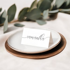 Puede incluir: Una tarjeta de lugar blanca con el nombre "Samantha" escrito en cursiva elegante en un plato blanco con una base de madera marr&oacute;n.