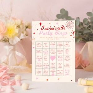 May include: A pink and red bachelorette party bingo card with a pink disco ball and a martini glass graphic. The card has a grid of 25 squares with different activities to complete, such as "trade shirts with someone", "dance on a table", "fake a proposal", "get a stranger to serenade you", "use a cheesy pickup line", "photo of you wearing a hat/boa", "do a tequila shot", "get a stranger to buy you a drink", "photo with someone in uniform", "sing karaoke", "kiss a stranger", "get a free drink", "body shot", "get a group to chant your name", "take a selfie with a bouncer", "get a piggyback ride", "take a shot with a stranger", "get a guy's phone number", "take a picture in a funny pose", "get a stranger to dance with you", "take a selfie in the men's bathroom", "wear a stranger's hat", "flirt with the bartender", "dance on a pole".