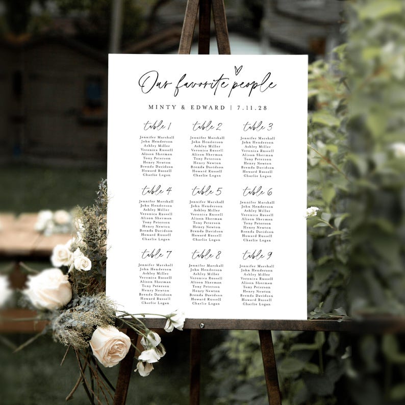 Elegant outdoor wedding seating chart sign titled "Our Favorite People" displayed on an easel, surrounded by white roses and rustic florals. A soft natural background enhances the romantic and minimal design, ideal for custom table assignment signage.