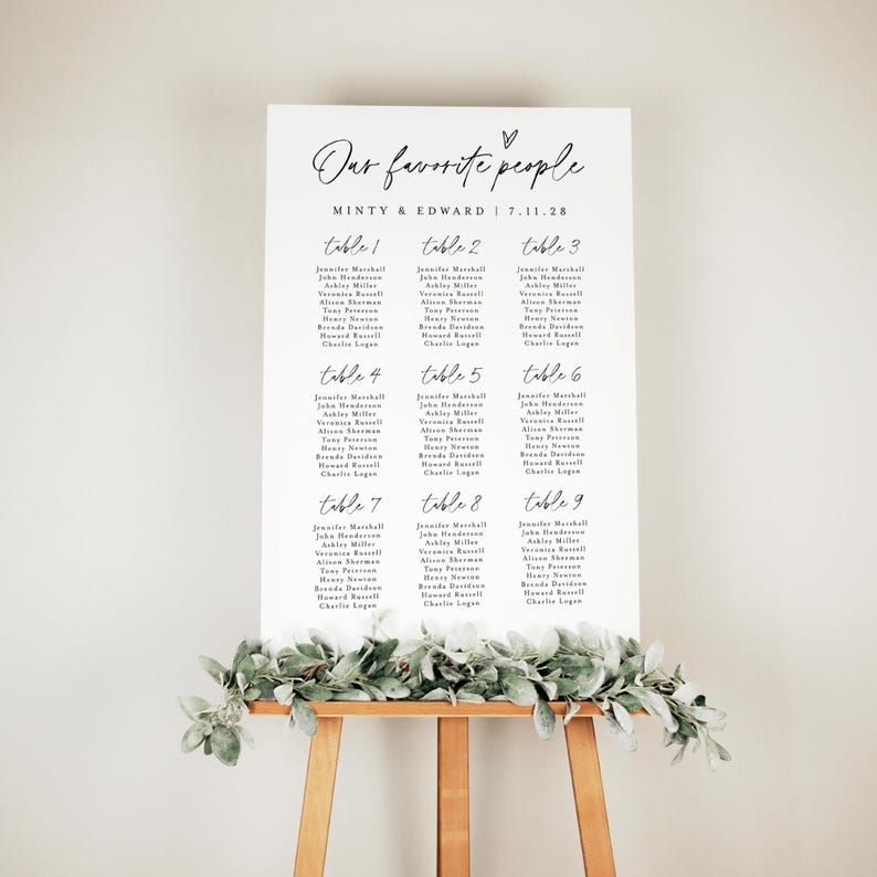 Wedding seating chart poster titled "Our Favorite People" styled with eucalyptus garland on a natural wood easel. Indoor setting with neutral tones emphasizes the soft, minimalist aesthetic for a timeless wedding sign.