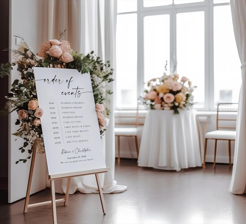 Puede incluir: Un caballete blanco que muestra un letrero de orden de eventos de boda, adornado con arreglos florales. El letrero presenta una caligraf&iacute;a elegante y un horario, que incluye la ceremonia, fotos y detalles de la recepci&oacute;n. El letrero est&aacute; en un espacio luminoso y espacioso con grandes ventanas.