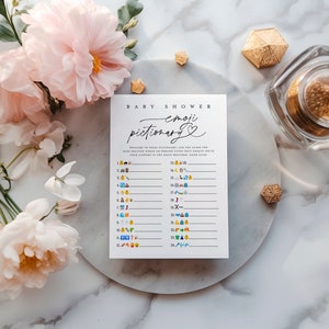 K&ouml;nnte beinhalten: Eine wei&szlig;e Karte mit dem Text "Baby Shower emoji pictionary" in schwarzer Schrift. Die Karte hat 24 nummerierte Zeilen mit Emojis auf der linken Seite und leere Zeilen auf der rechten Seite zum Schreiben von Antworten.
