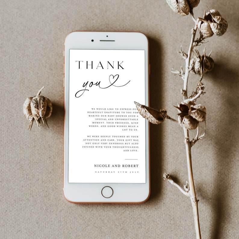 May include: A white smartphone with a black screen displaying a thank you message for a baby shower. The message reads "Thank you" with a heart symbol and expresses gratitude for the guests' presence and gifts. The message is signed "Nicole and Robert" and the date "Saturday 17th July".