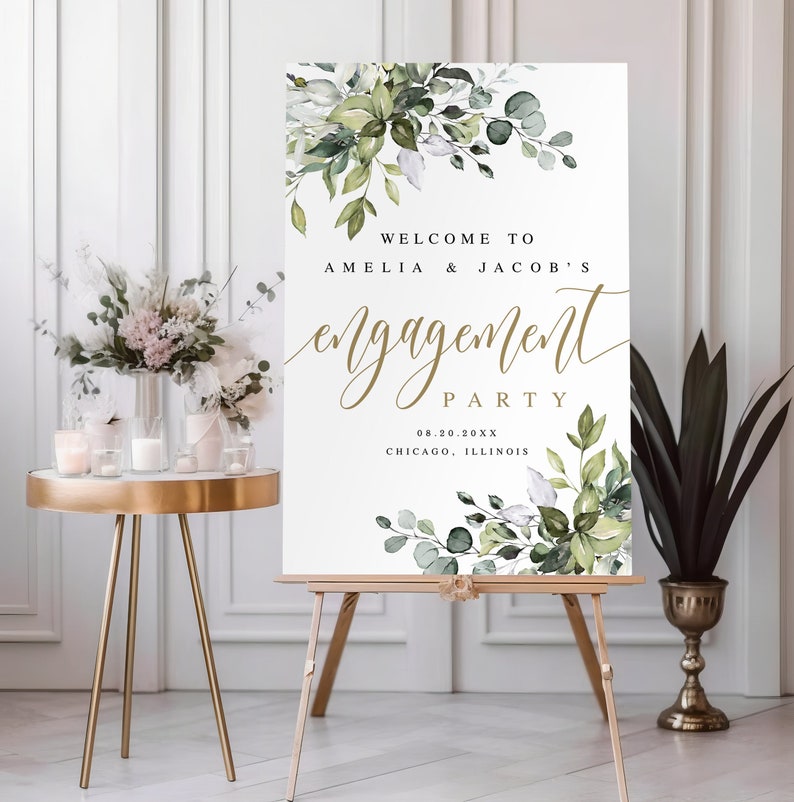 Puede incluir: Un cartel de bienvenida blanco con follaje verde acuarela y letras doradas. El cartel dice "Bienvenido a Amelia & Jacob's Engagement Party 08.20.20XX Chicago, Illinois".