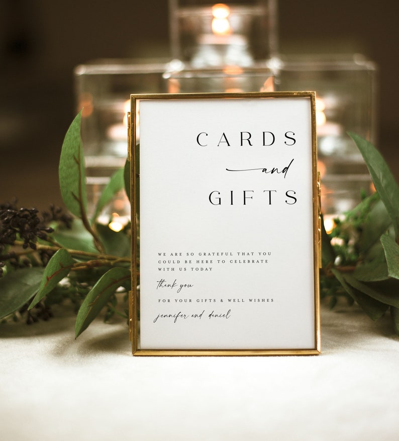 May include: A gold-framed sign with white background and black text that reads "CARDS and GIFTS". The sign also includes the text "WE ARE SO GRATEFUL THAT YOU COULD BE HERE TO CELEBRATE WITH US TODAY. Thank you FOR YOUR GIFTS & WELL WISHES jennifer and daniel."