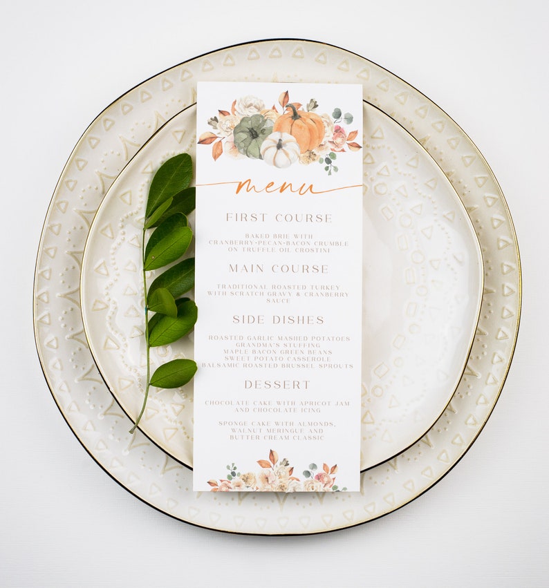 Op de afbeelding: Een printbare Thanksgiving-menukaart met een aquarel-illustratie van pompoenen en herfstbladeren. Het menu bevat een voorgerecht, een hoofdgerecht, bijgerechten en een dessert.