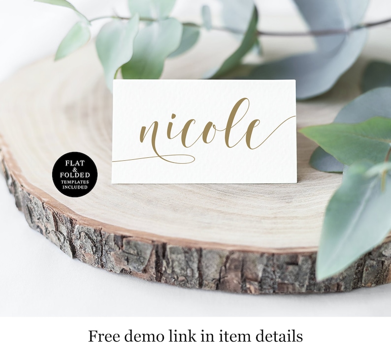 以下が含まれることがあります： 木製の円盤の上に、「nicole」という名前が金色の筆記体で書かれた白いカード。カードは木の表面に置かれ、背景には緑の葉が見える。