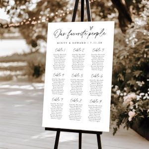 Chic outdoor "Find Your Seat" wedding seating chart sign on black easel, surrounded by soft lighting and floral decor. Scripted headers and modern typography make this Templett.com editable chart perfect for receptions.