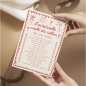 May include: A white card with red decorative border and text, held by hands. The card reads "Bachelorette would she rather" with a list of playful questions. The card has illustrations of a champagne bottle, disco ball, and wine glasses.