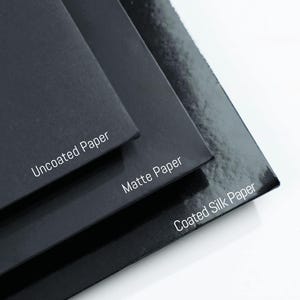 May include: Close-up of three black paper samples: Uncoated Paper, Matte Paper, and Coated Silk Paper. The paper samples are stacked, showcasing different textures and finishes. The text is in white.