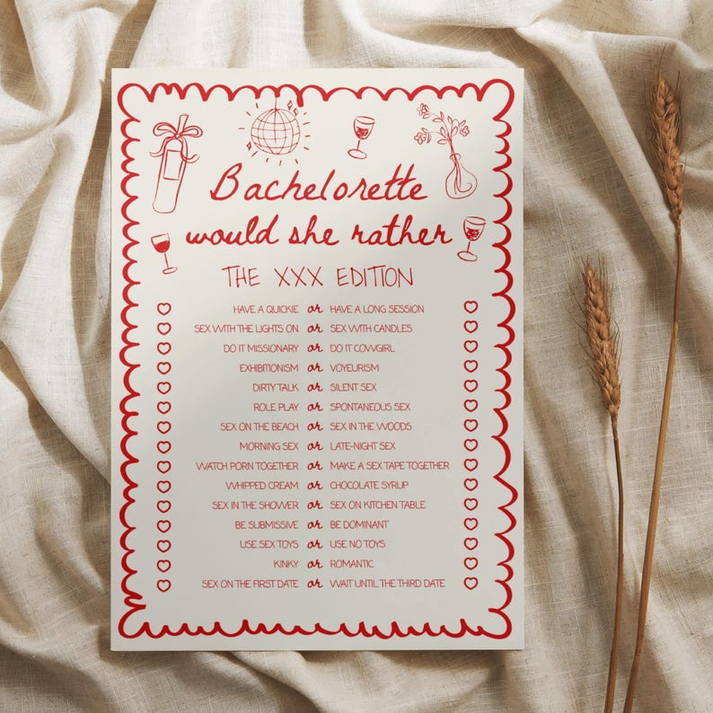 May include: A white card with red border and text that reads "Bachelorette would she rather THE XXX EDITION". The card has red illustrations of a disco ball, wine glasses, and flowers. The card is on a beige fabric background.