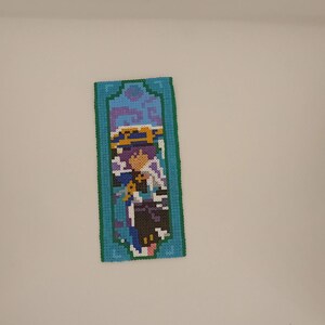 May include: A blue and purple pixel art tapestry featuring a character with a blue hat and a purple and blue outfit.