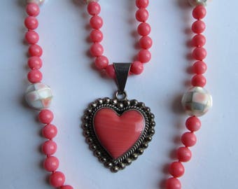 May include: A pink coral necklace with a silver heart pendant. The necklace is made of pink coral beads and silver beads. The heart pendant is made of pink coral and silver.
