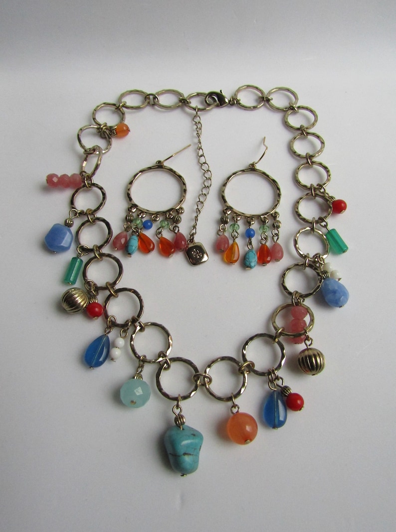 May include: A gold chain necklace with multiple colorful beads and charms, including turquoise, blue, red, orange, and pink. The necklace is paired with matching earrings with similar charms.