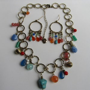 May include: A gold chain necklace with multiple colorful beads and charms, including turquoise, coral, and blue glass. The necklace is paired with matching earrings with similar charms.