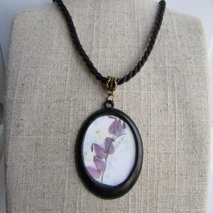 May include: A black cord necklace with a round pendant featuring a pressed flower and the text "wild heart".