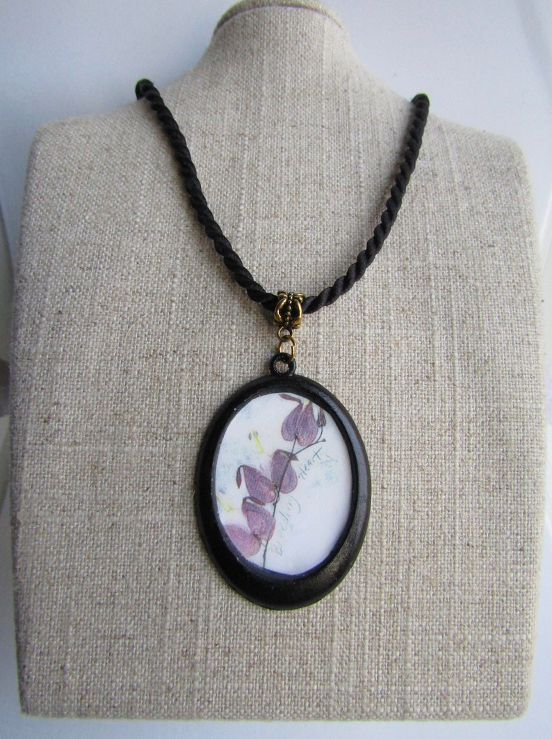 May include: A black cord necklace with a round pendant featuring a pressed flower and the text "wild heart".