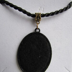 May include: A black oval pendant necklace with a gold-toned clasp. The pendant is made of a smooth, black material and hangs from a black cord.