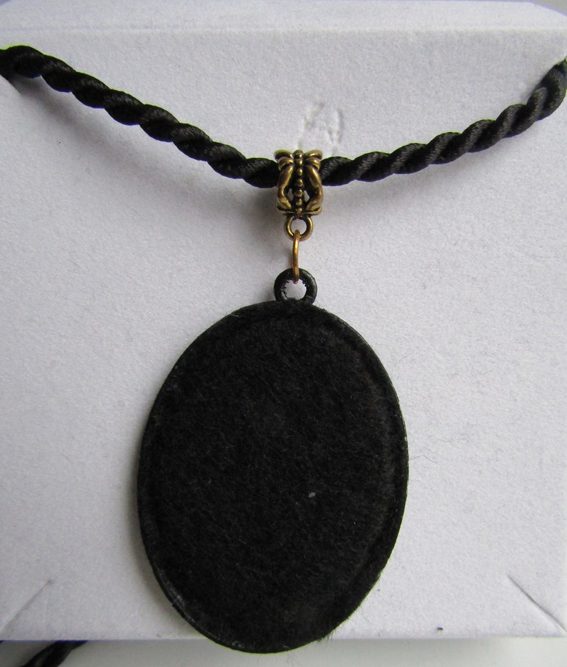 May include: A black oval pendant necklace with a gold-toned clasp. The pendant is made of a smooth, black material and hangs from a black cord.